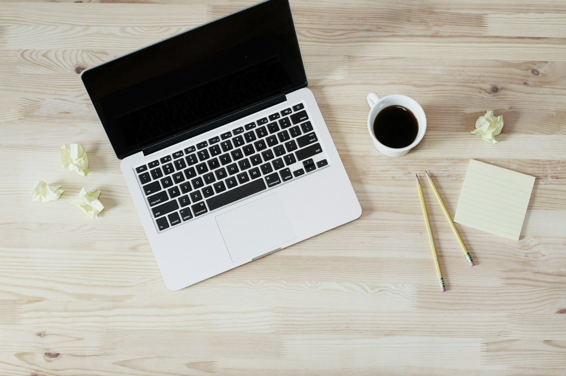 Laptop, coffee, pencils, and note card arranged on a bright desk for preparing an email signature
